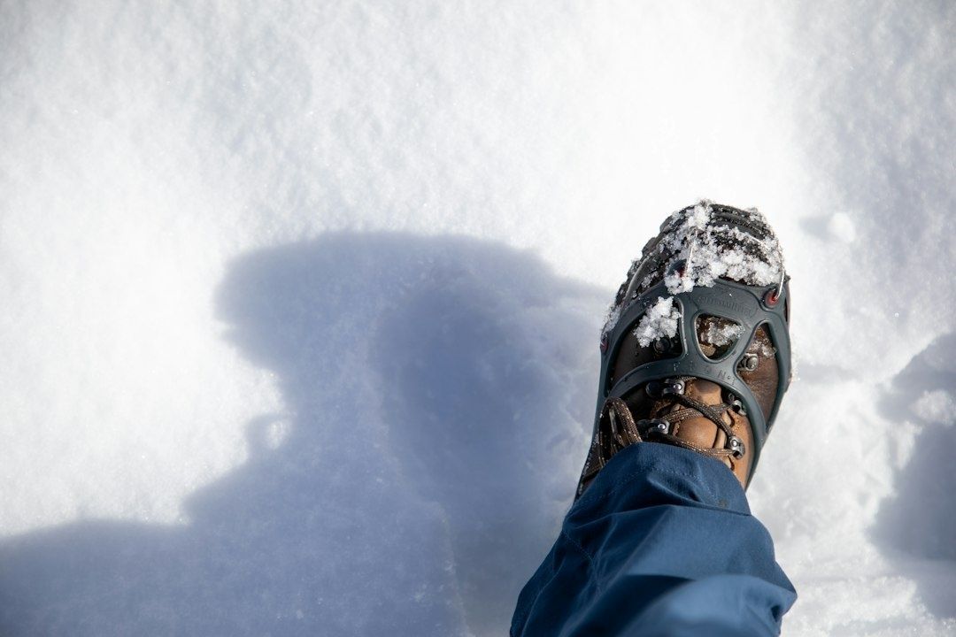 Nærbilde av brodder på en sko som tråkker i snø