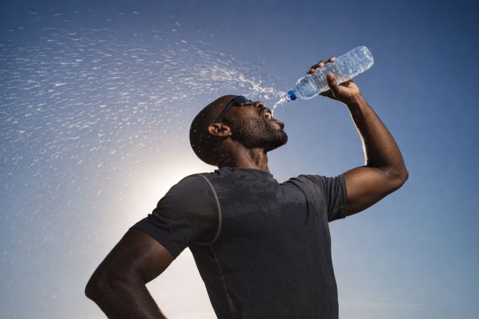 En løper som drikker vann for å holde seg hydrert under trening ute i solen.